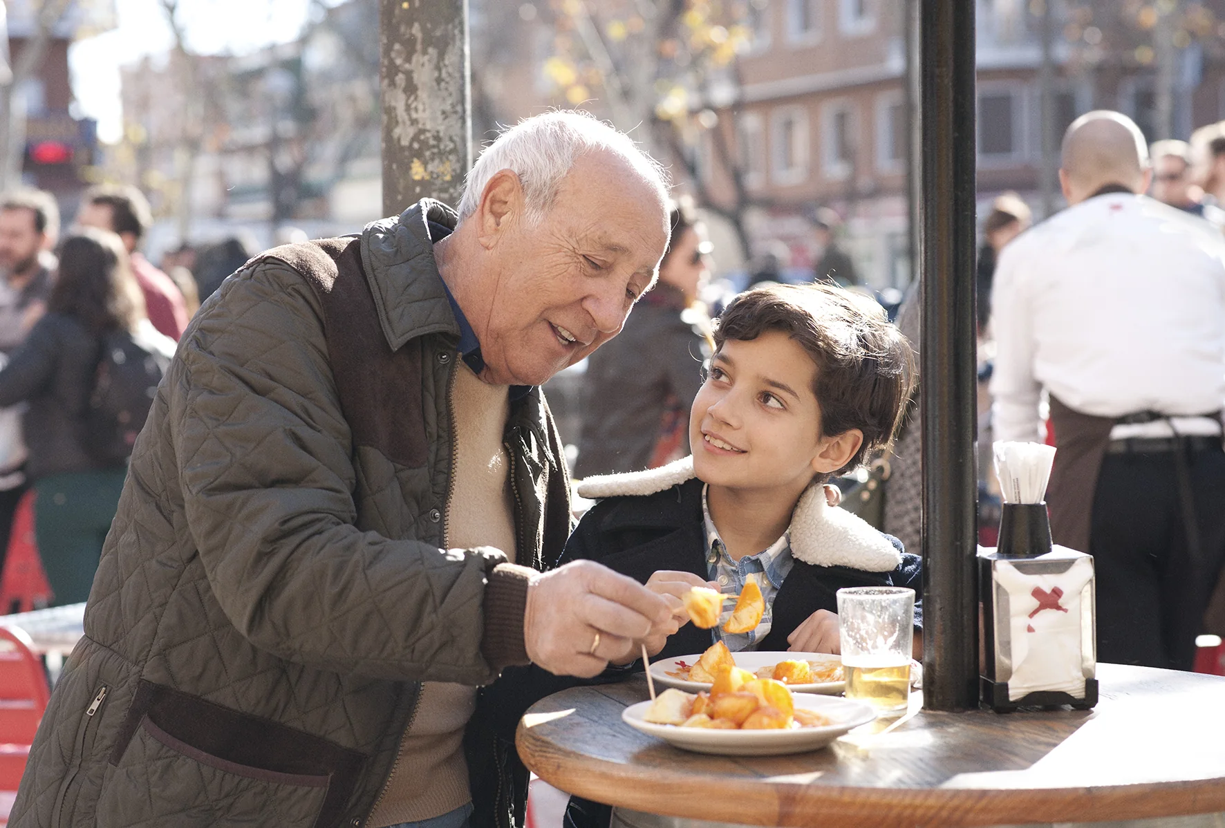 Un abuelo y su nieto compartiendo patatas bravas en la terraza de Docamar