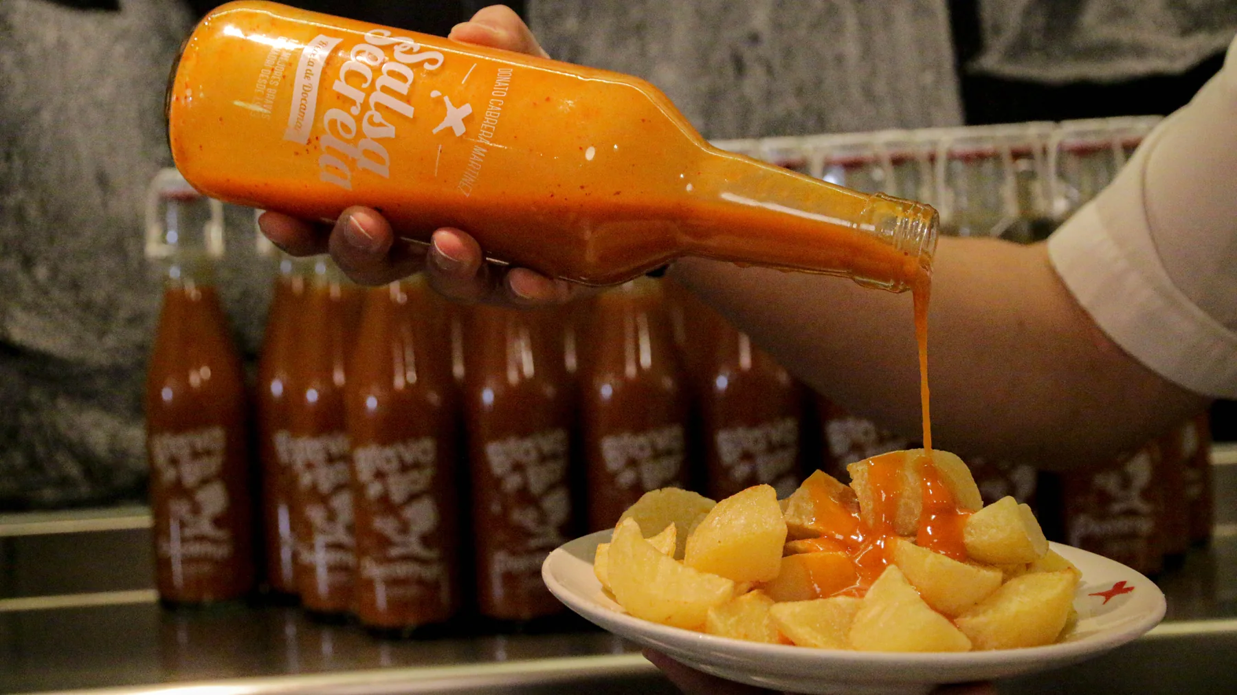 Salsa brava de Docamar cayendo desde la botella sobre una ración de patatas